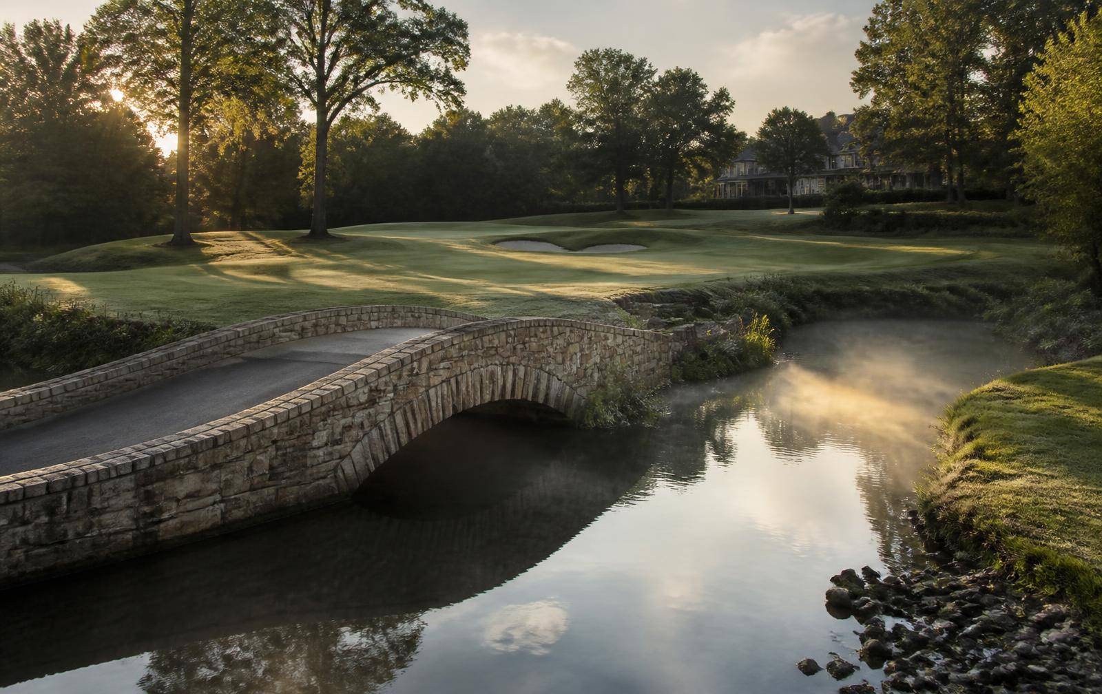 Stone cart bridge crossing a misty creek on a private golf course at dusk