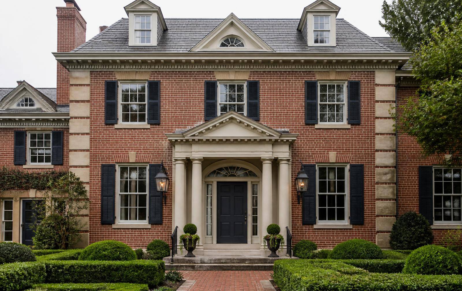 Red brick estate facade with limestone quoins, black shutters and a pedimented portico
