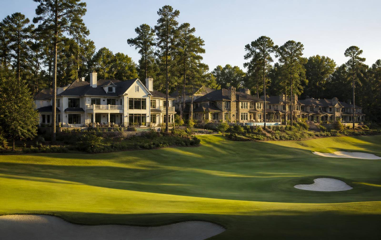 Large custom homes with rear terraces overlooking a manicured golf fairway at golden hour