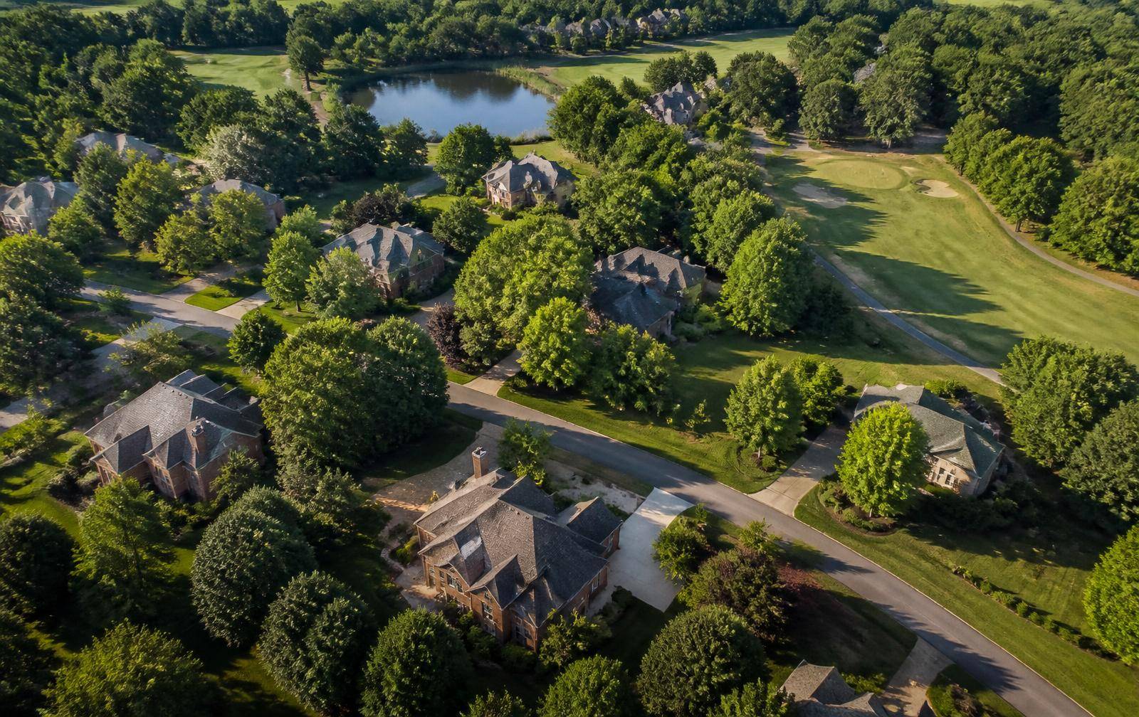 Aerial view of large rooftops among mature tree canopy beside golf fairways and a pond