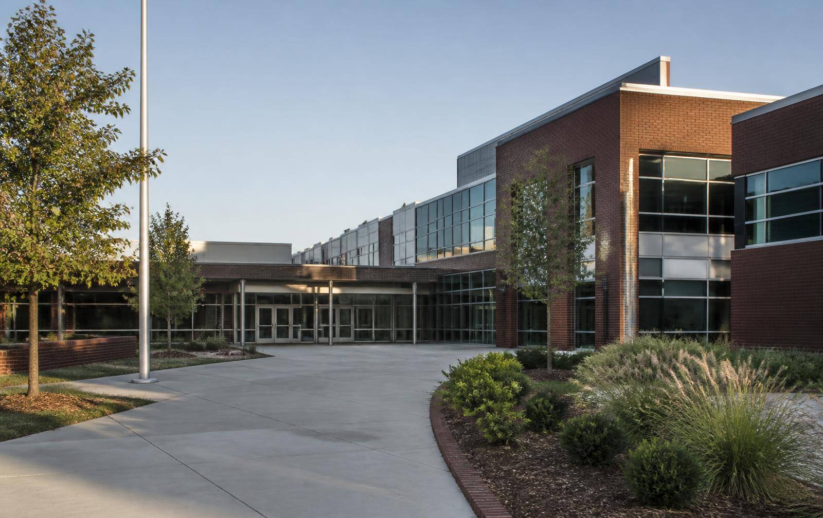 Modern brick and glass school campus entrance with landscaped courtyard in morning light